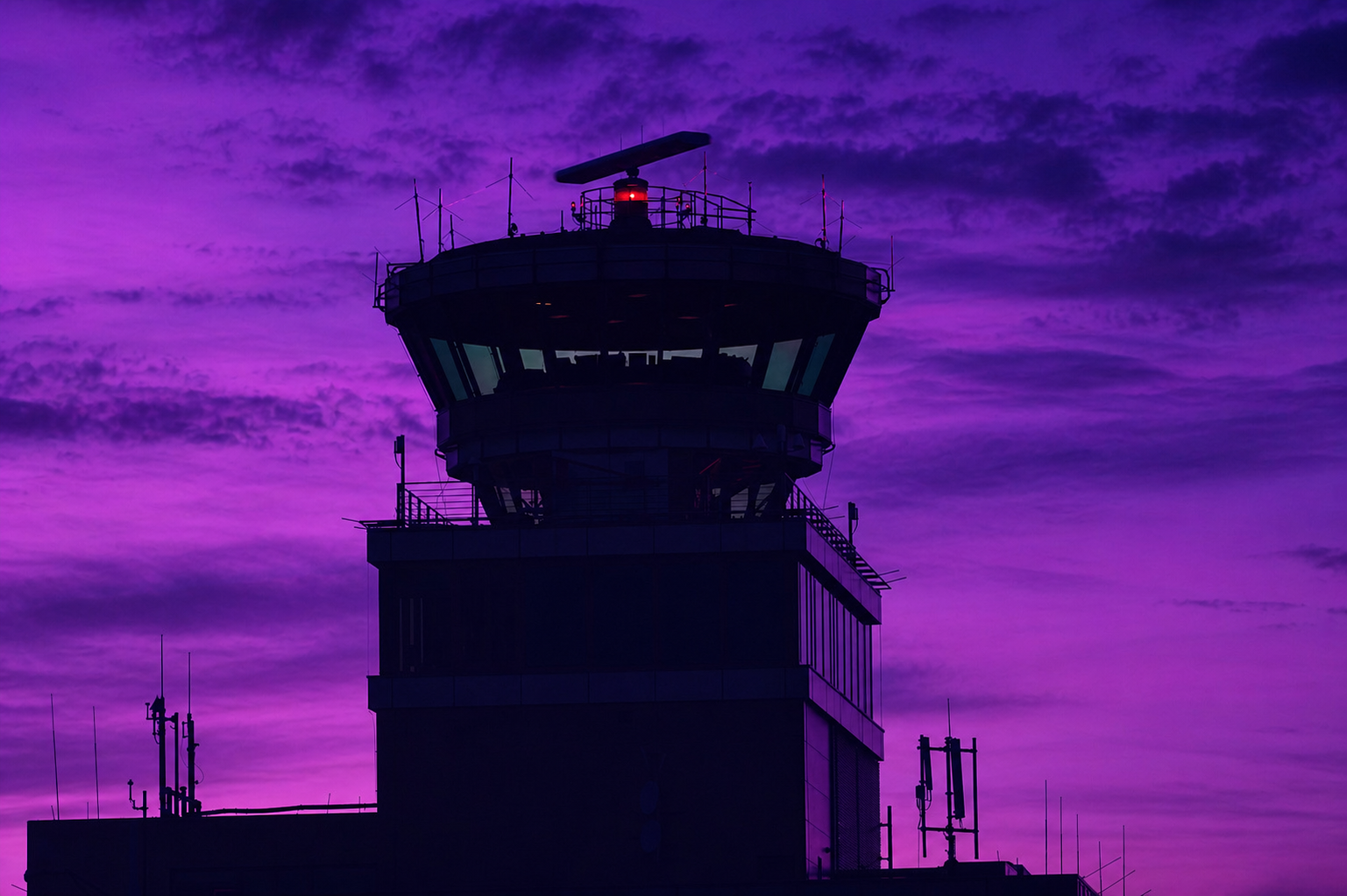 Air traffic control tower silhouetted against a deep purple dusk sky, radar rotating above the cabin.